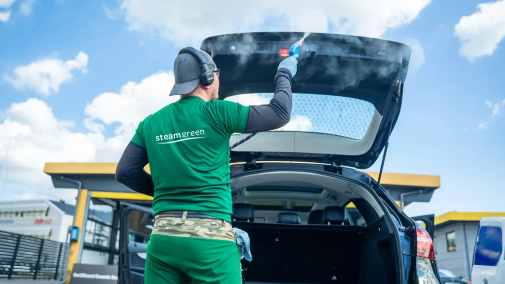 Steamer i grøn SteamGreen-trøje damper bagklappen på en bil indefra